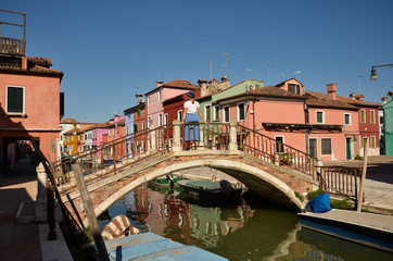 Fototapeta na wymiar Scenic canal with colorful buildings in Burano island, Venice, Italy. Woman tourist