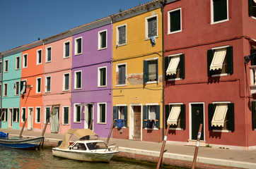 Fototapeta na wymiar Colourful painted houses along the canal on the island of Burano, Venice, Italy. The island is a popular attraction for tourists due to its picturesque architecture