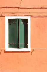Green window with shutters on orange wall. Colourful painted windows. Burano island near Venice, Italy. Abstract background, texture