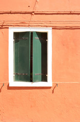Green window with shutters on orange wall. Colourful painted windows. Burano island near Venice, Italy. Abstract background, texture