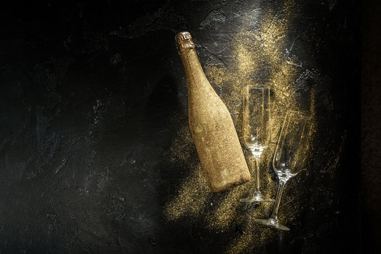 Romantic photo of golden champagne bottle, two wine glasses on black stone background