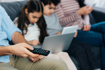 selective focus of remote contol in hand of man near hispanic hamily using gadgets
