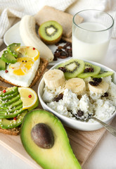 cottage cheese with banana slices, kiwi, raisins, avocado sandwich, milk