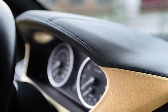 Speedometer and tachometer on dashboard of an luxury car closeup, covered with natural beige and black stitched leather