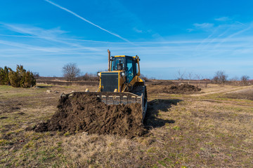 Fototapeta premium A big yellow bulldozer pushes the ground and makes a new road