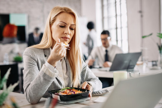 Businesswoman Eating Salad At Her Desk In The Office.