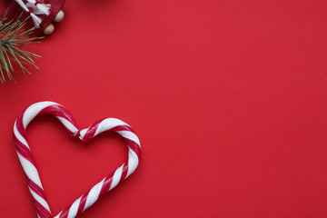Christmas candy canes heart-shaped isolated on red background. Red and white candy canes and fir-tree branch on red background.