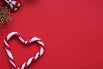 Deurstickers Christmas candy canes heart-shaped isolated on red background. Red and white candy canes and fir-tree branch on red background. © Marharyta