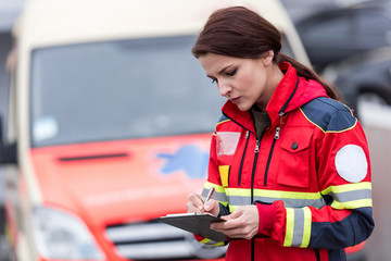 Concetrated female paramedic in uniform writing in clipboard