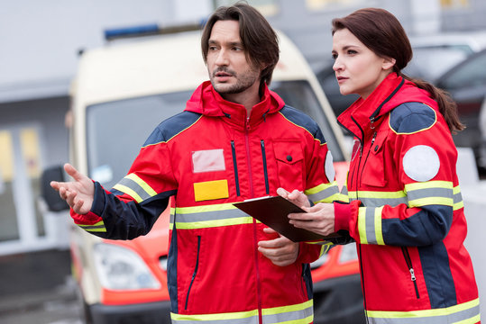 Paramedics in red uniform talking and looking away on street
