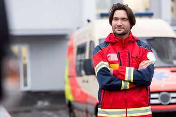 Confident paramedic in red uniform standing on street with crossed arms
