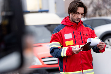 Concentrated paramedic in red uniform writing in clipboard