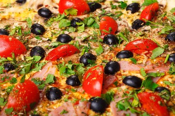 Close up Italian pizza with melted cheese, red cherry tomatoes, black olives, ham, and green leaves on a brown table decorated with mushrooms, red hot chili pepper and cherry tomatoes