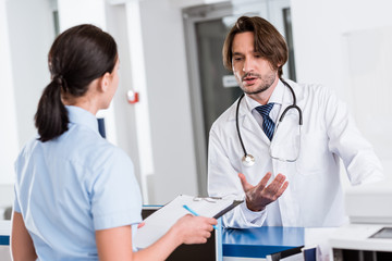 Fototapeta na wymiar Handsome doctor in white coat talking to nurse