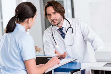 Serious doctor with stethoscope talking to nurse in clinic