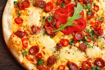 Top view close up Italian pizza with melted cheese, sausage, snack sticks, pepper and fresh green oregano leaves on a brown table decorated by mushrooms, red sweet pepper and cherry tomatoes