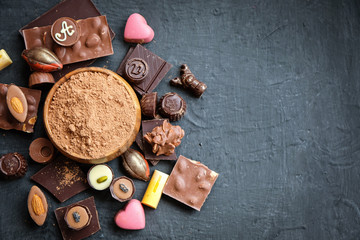 Assorted chocolate and cocoa powder on black background