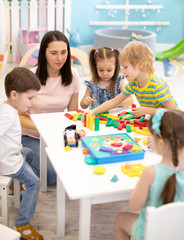 Little children playing different toys with teacher in daycare. Kids building color blocks. Educational toys for preschool and kindergarten pupils.