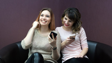 Close friends sit on the couch talking to each other and on the Internet.