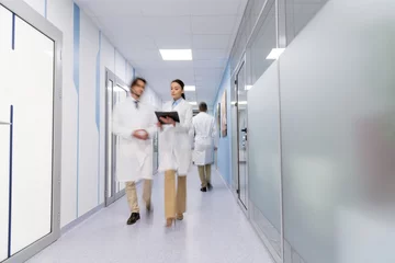 Fotobehang Doctors in white coats with black folder walking down hall © LIGHTFIELD STUDIOS