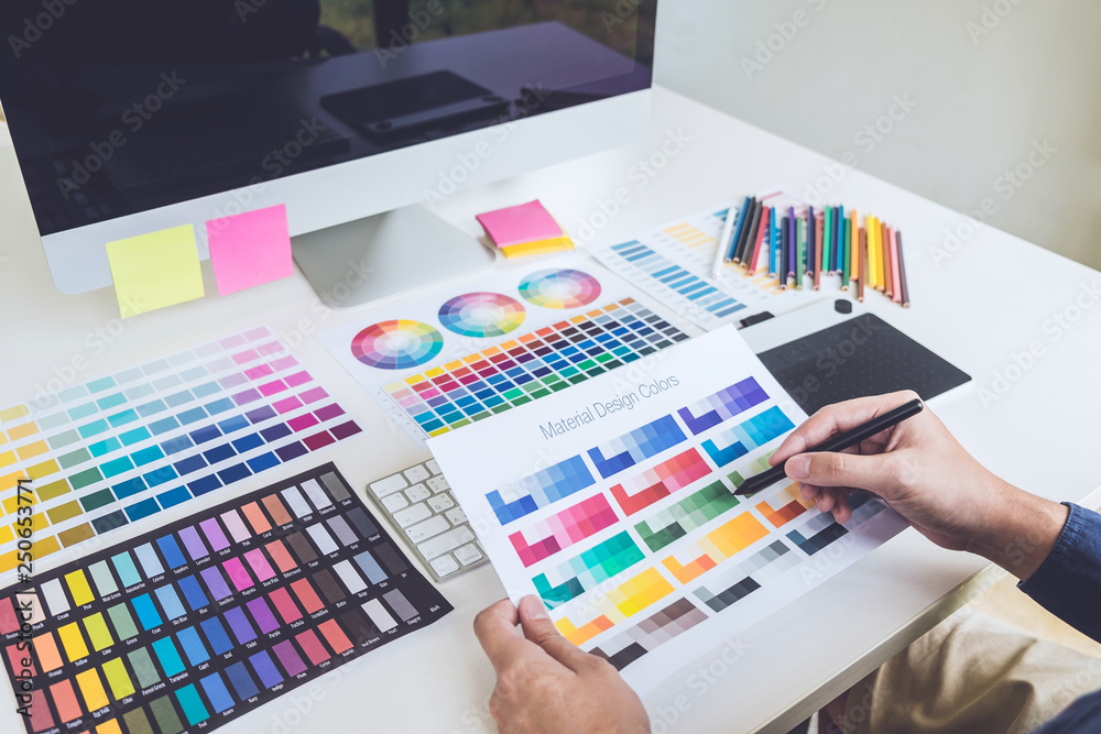 Poster Image of male creative graphic designer working on color selection and drawing on graphics tablet at workplace with work tools and accessories