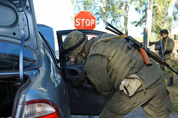 At the checkpoint, training. Soldiers searching personal belongings of suspect in a stopped car
