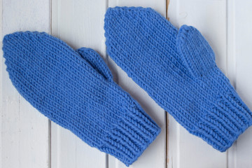 Warm knitted mittens and gloves on the white wooden background