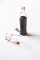 Homemade Cherry Syrup/Liqueur in a little bottle and in a shot glass, on white background.
