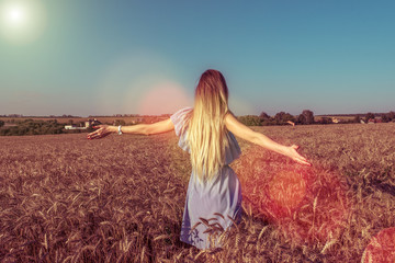 The girl in the dress view from back, walks in the summer in a wheat field. With long dyed hair, arms spread apart. The concept of freedom of joy of discovery and fresh air in nature.