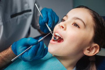 Calm peaceful girl sit in dental chair in room. She keep mouth opened. Dentist use tools for check up.