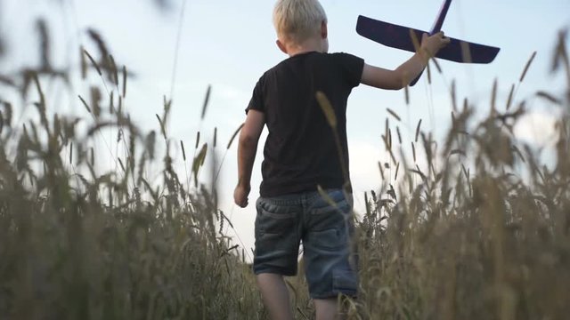 A boy with an airplane in his hands is running in the field