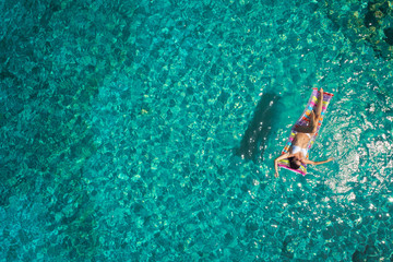 Aerial view of young woman swimming on the pink inflatable mattr.