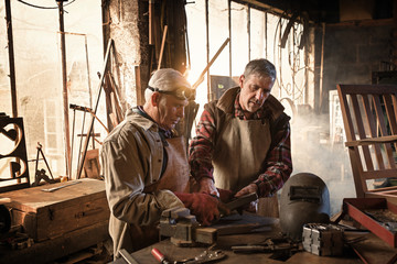 Two craftsmen in their craft workshops work metal parts 