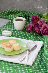 Delicious Dietary Cheesecakes from Homemade Farmer's Cheese for breakfast, black coffee and a bouquet of purple tulips on a green tablecloth.