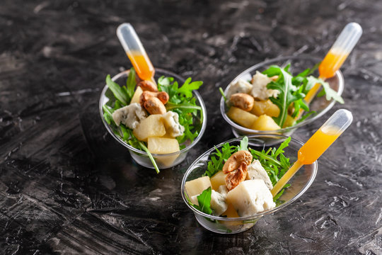 Modern European appetizer. Mini salad with gorgonzola, pear and roasted cashews. Orange dressing in sauceboat, capsule, pipette. Dish in disposable tableware. trend 2019