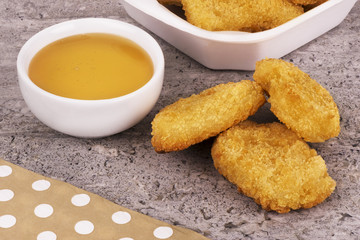 Chicken nuggets with a sweet sauce bowl's disposed on a concrete background. Fast food concept.