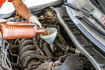 Car mechanic replacing and pouring fresh oil into engine at maintenance repair service station .