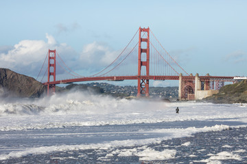 View of the Golden Gate Bridge from Baker beach with man fishing in huge waves.