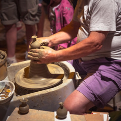 Potter makes a clay pot, sitting outside surrounded by people watching