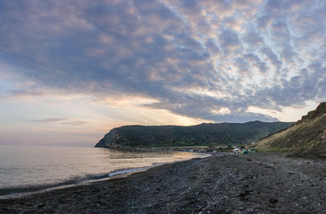 Orange-blue sky at sunset,calm sea level, pebble beach and hills and cliffs on background. West coast of island Limnos, Greece