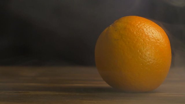 Juicy orange on a black background in the smoke and coolness, close-up, slow motion, copy space