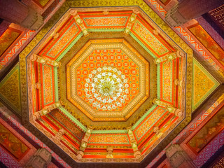 Beautiful chandelier lamp is hanging on the decorated ceiling in the Buddhist church, Thailand. Colorful pattern of ceiling with decorative chandelier lamp.