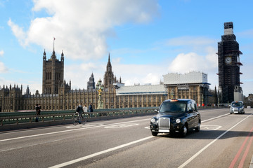 Fototapeta na wymiar Black cabs drive on the London street with illuminated taxi sign