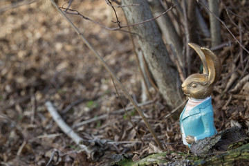 Osterhase in blauem Frack im Frühlingswald zwischen braunen Blättern und Ästen am Waldboden