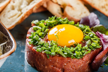 Beef tartare served with an egg yolk, chopped green onions, toast and butter in plate on dark stone background. Clean eating, healthy food concept