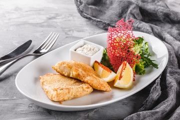 Fried fish fillet with salad and lemon in plate over rustic background. Hot fish dish