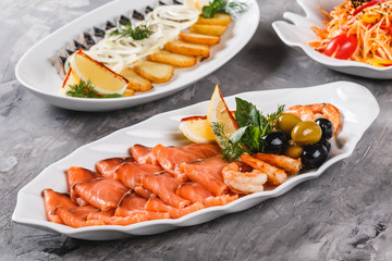 Seafood platter with salmon slice, shrimp, slices fish fillet, decorated with olives and lemon in plate over rustic background. Mediterranean appetizers