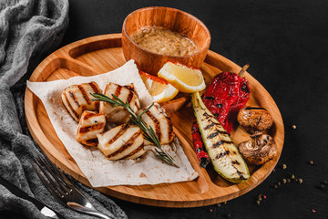 Grilled fillet fish and vegetables with spice sauce on cutting board over black stone background. Hot fish Dishes. Top view, flat lay