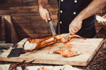 Chef Hands cutting grilled rabbit for steaks with knife on cutting board. Hot Meat dishes