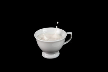 Tiny coffee cup filled with milk with a splash creating a drop of milk floating in mid air above the cup isolated against a black background